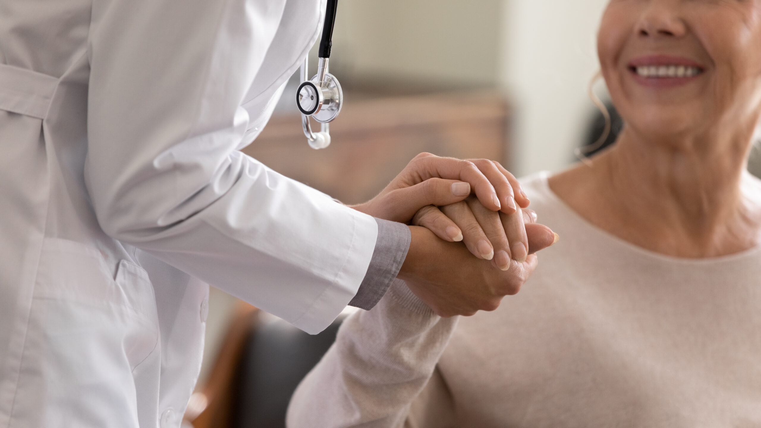 Young female physician holding hand of smiling elderly lady patient doctor with a geriatric patient